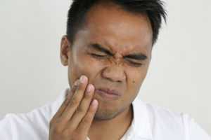 Man wincing in pain from a tooth ache and looking for an emergency dentist.