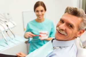 Older man sitting in dentist chair smiling from getting his new teeth-in-a-day.